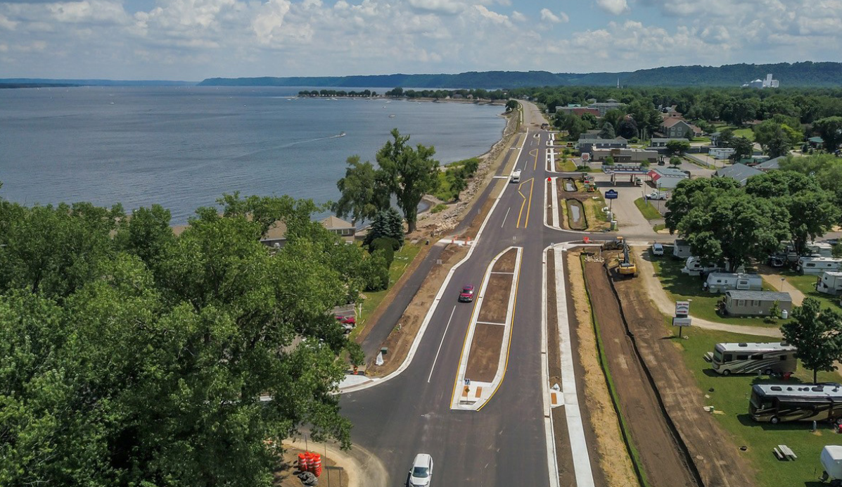 An image taken by a drone of Highway 61 in Lake City MN, showing shared-use path, sidewalk, and medians. The road is next to a lake and there are trees surrounding the area.