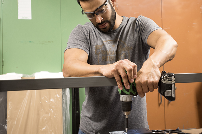 Man wearing safety glasses using a power drill on equipment indoors