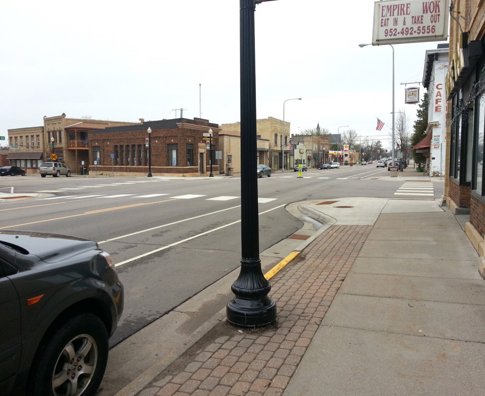 Hwy 28 (Minnesota Ave.) after construction, showing lane reduction to two traffic lanes and a center turn lane, raised cycletrack, bumpouts, and improved crosswalk