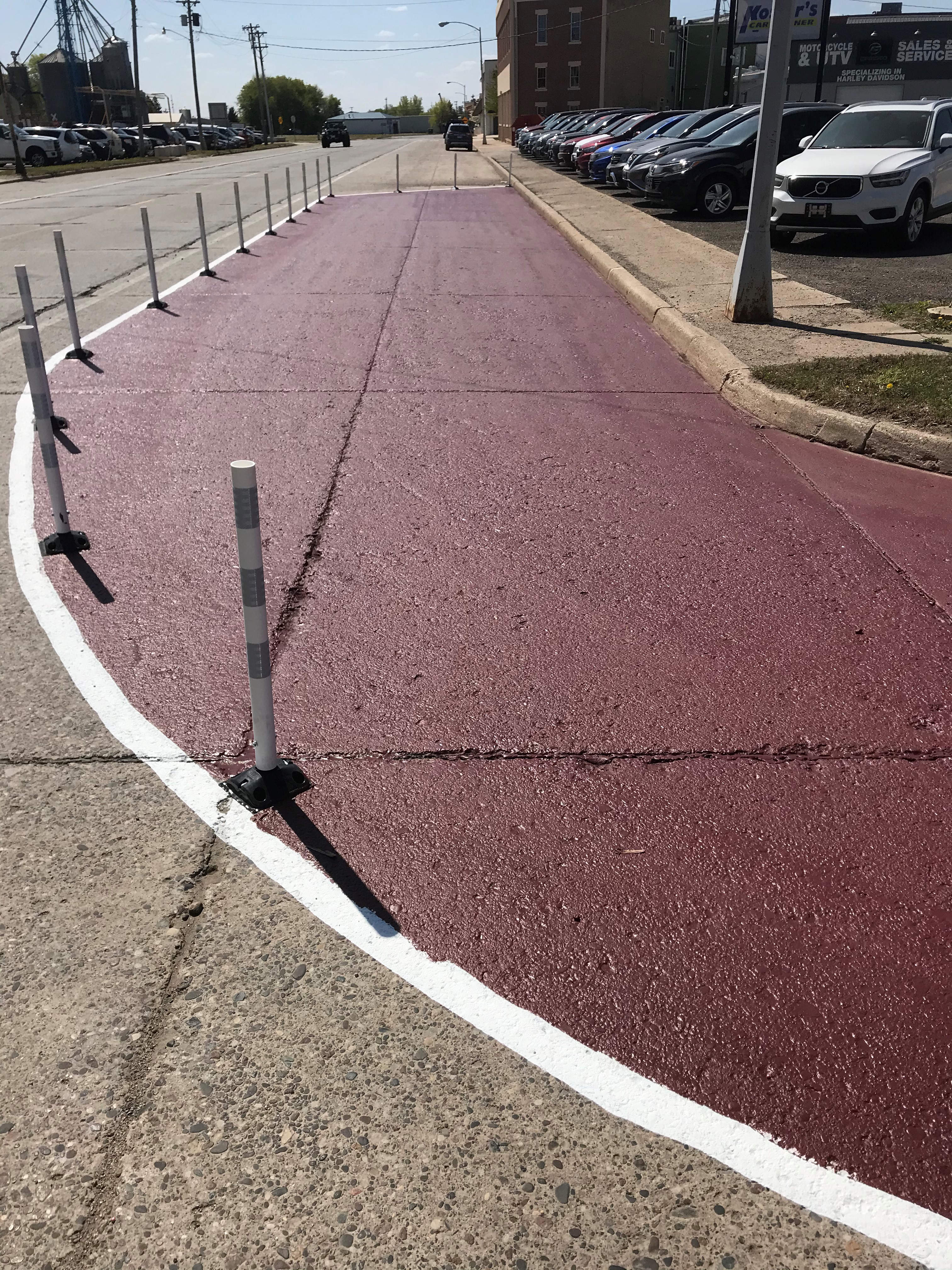 Portion of the road painted maroon with vertical posts indicate where the proposed new curb would be installed