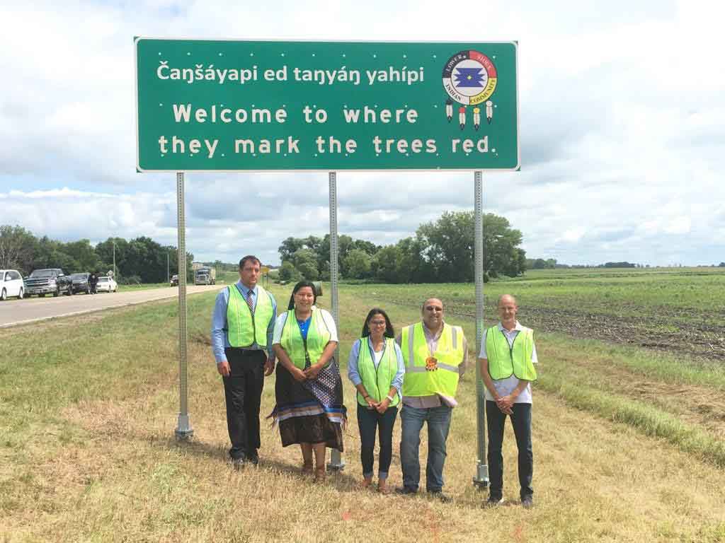 Lower Sioux Indian Community tribal council ceremonial unveiling of their dual language sign. Shown in the photo are the Lower Sioux Indian Tribal Council members. Included on the road sign is the Lower Sioux Indian Community tribal logo. Dakota text Cansa'yapi ed tanya'n yahipi which translates to Welcome to where they make the trees red in english.