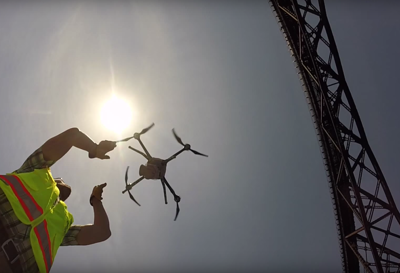 Person catching drone while landing with bridge and sun in background