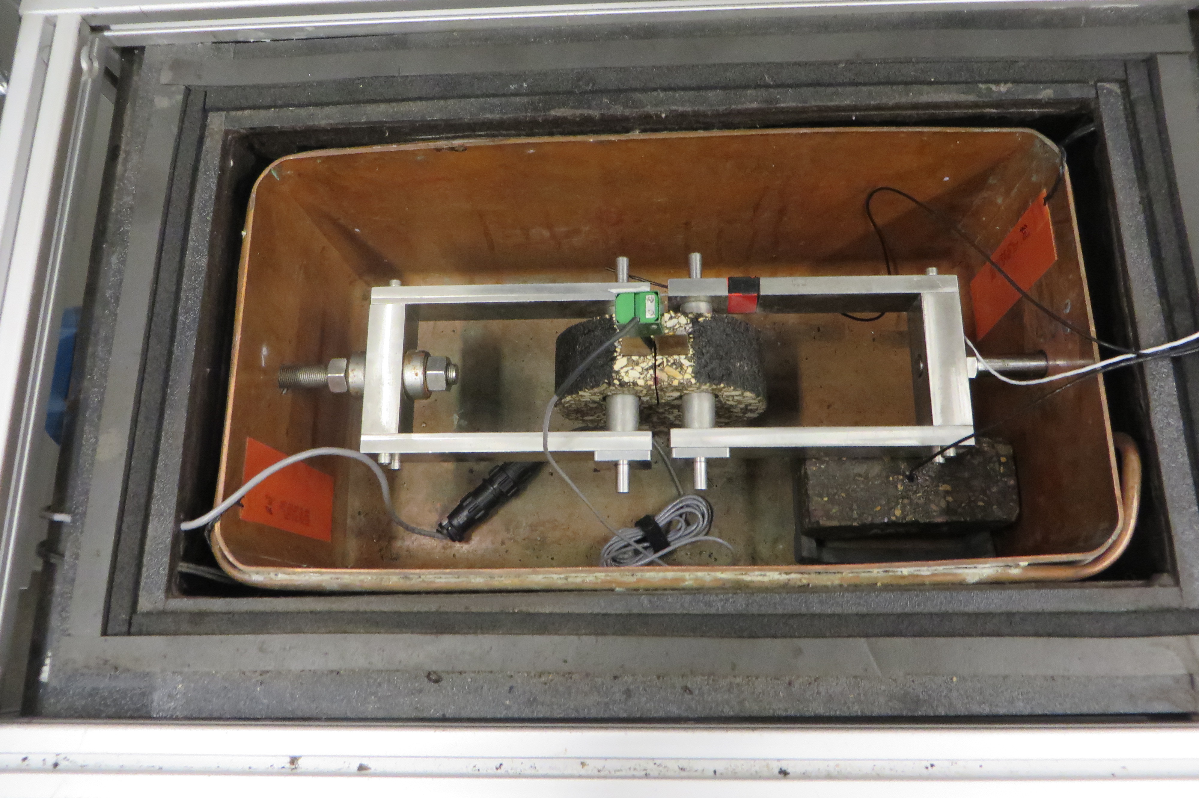 For the DCT test, a disc-shaped asphalt sample was instrumented with a temperature sensor and prepared for pulling tension to simulate its cracking susceptibility while contracting at low temperatures.