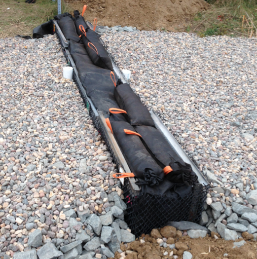 The iron-enhanced filter installed in this ditch check holds iron filings and sand in a geotextile fabric envelope and is supported by a metal filter cage extending across the swale. Topsoil and sod will cover the entire ditch check.