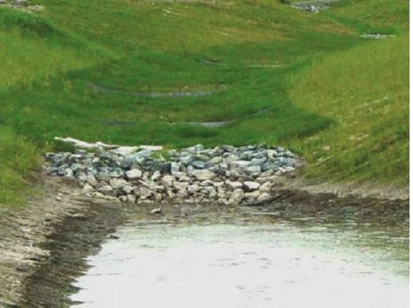 Two bioslopes lead to a bioswale. Stormwater follows the bioswale and is filtered through a stone outlet into a detention pond.