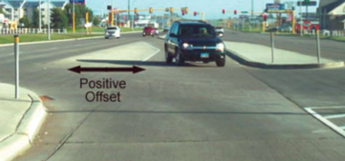 A vehicle waits in a left turning lane, separated by the main traffic lane by a concrete apron.