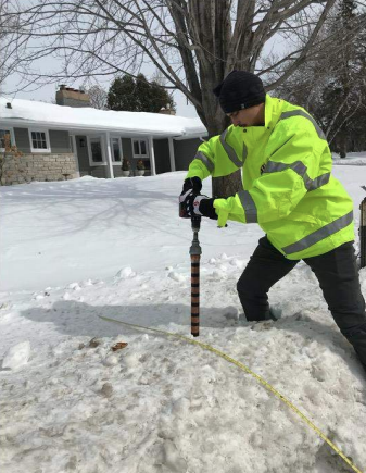 A researcher pushes a coring device into a snowbank along a city street.