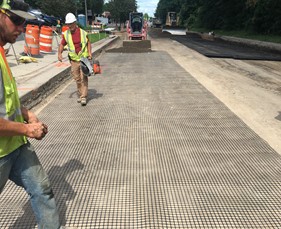 Two crewmembers walking on synthetic geogrid material, over an aggregate subgrade.
